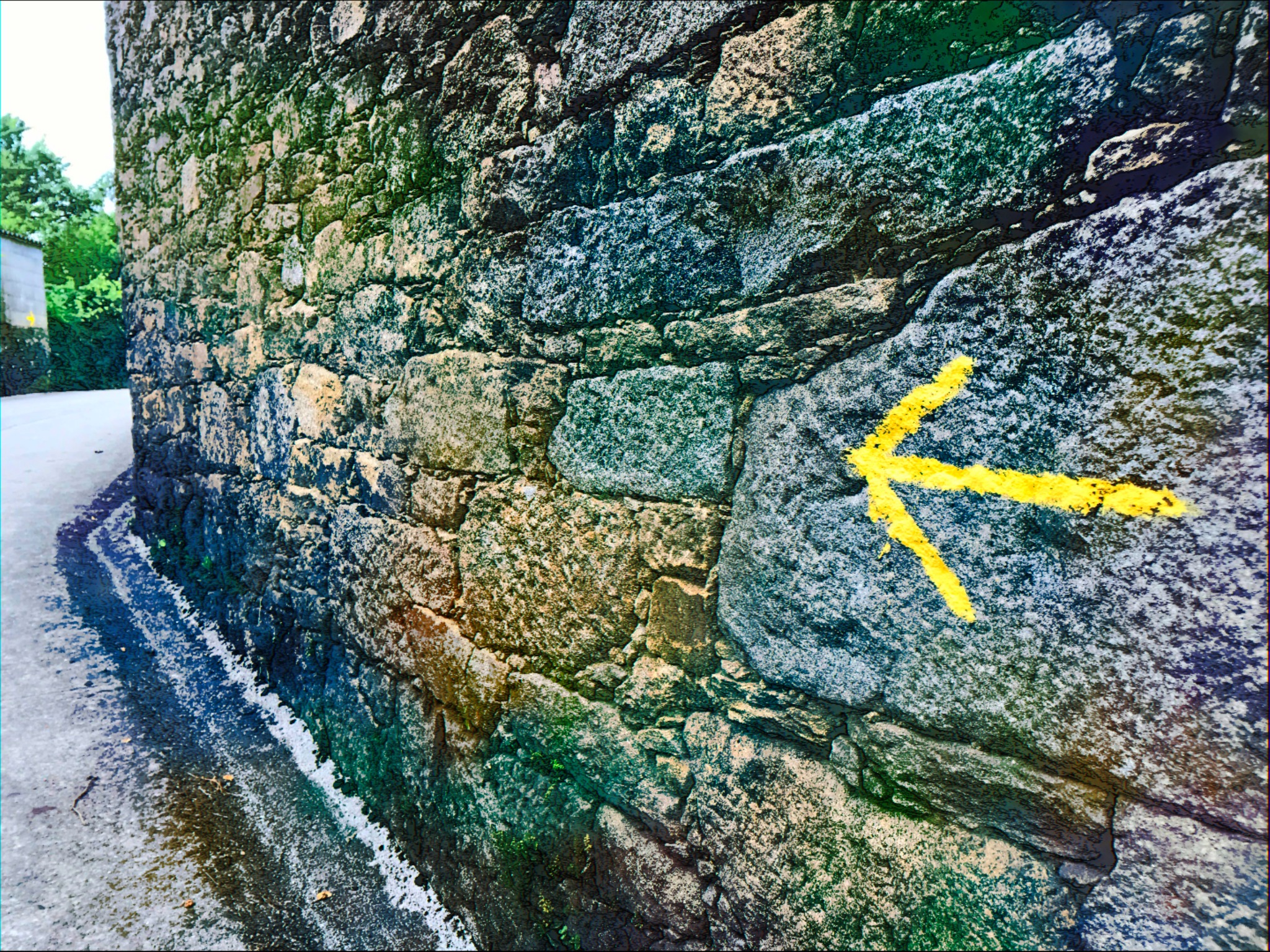 Gelber Camino-Pfeil an einer Steinmauer