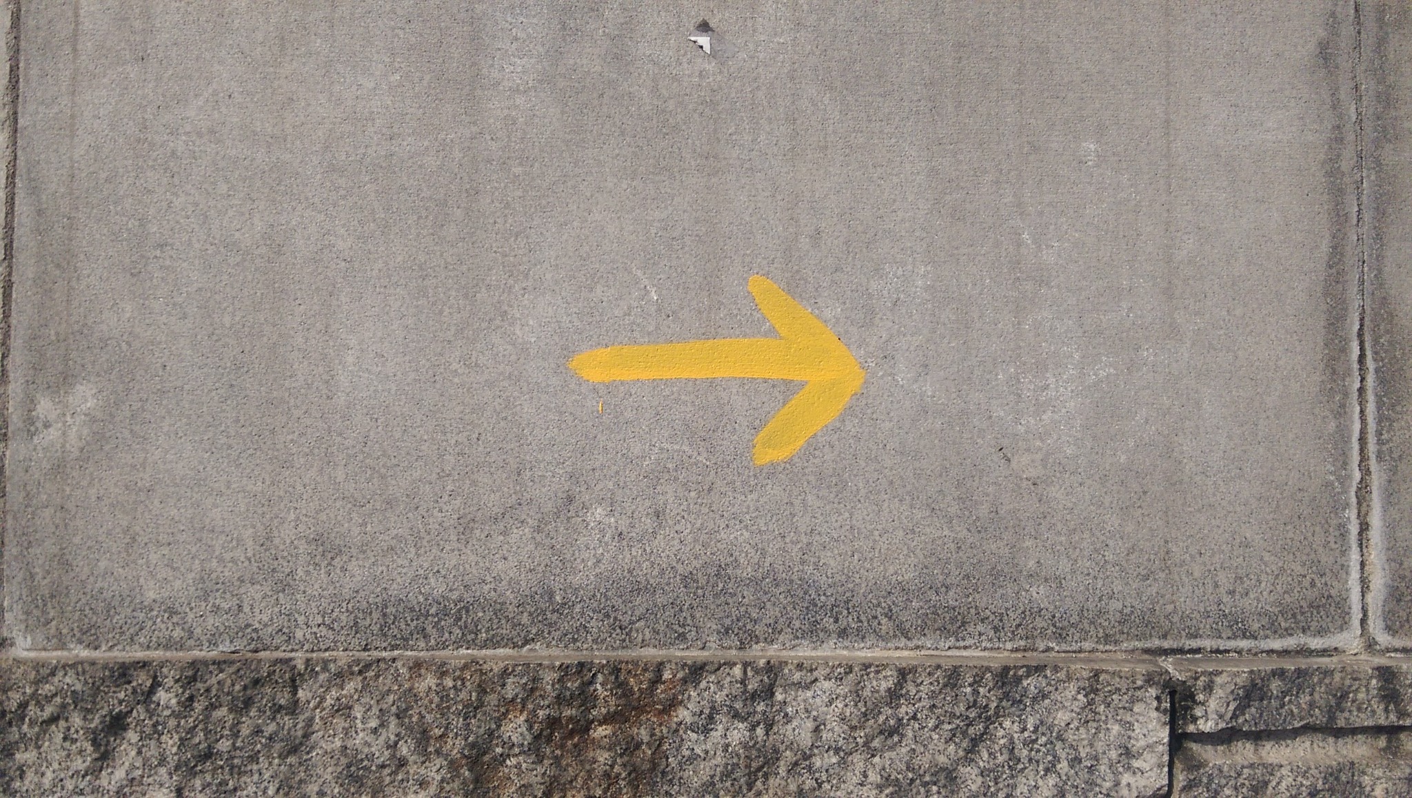 Gelber Camino-Pfeil auf einer Mauer